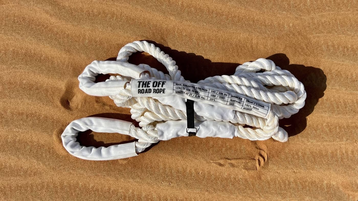 The Off Road Rope kinetic recovery rope with white sleeves and rating label, coiled on desert sand