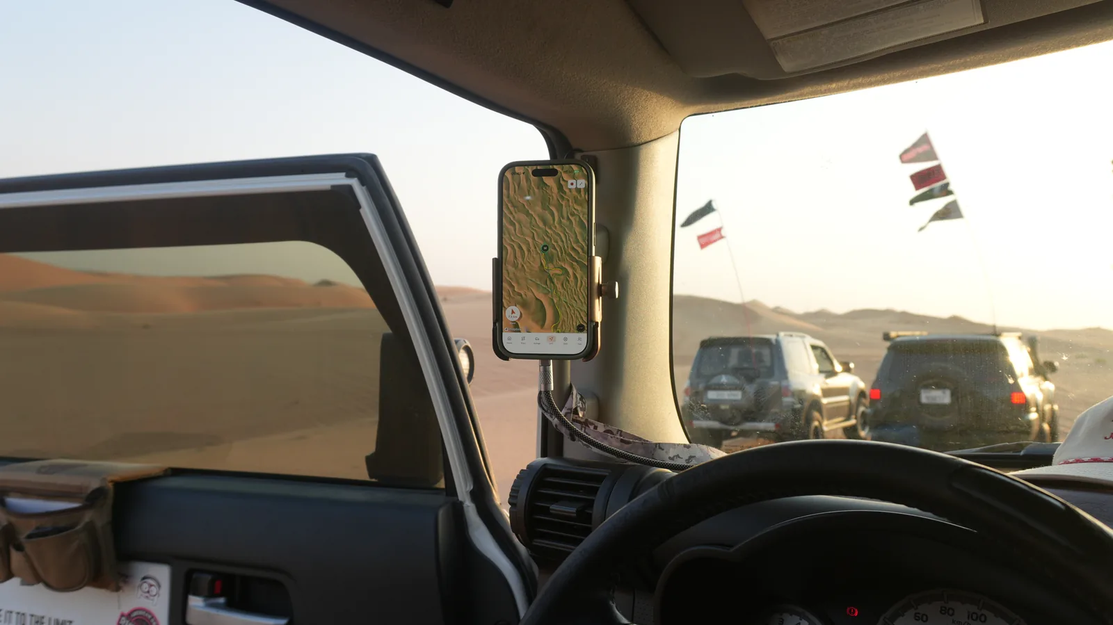 Mounted phone showing Navra terrain mapping and a track line, with convoy vehicles beyond the windscreen