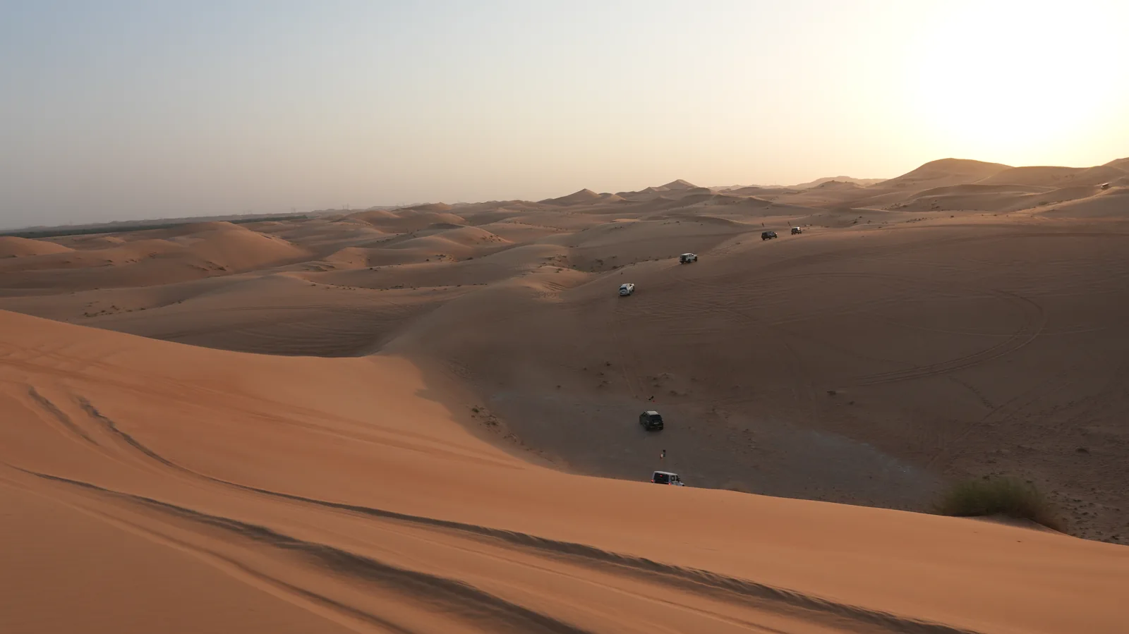 A line of 4x4 convoy vehicles spread across the desert dunes in morning light