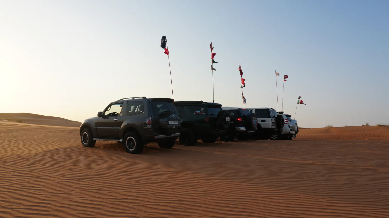 Flagged 4x4 convoy parked together on the sand during a UAE desert drive